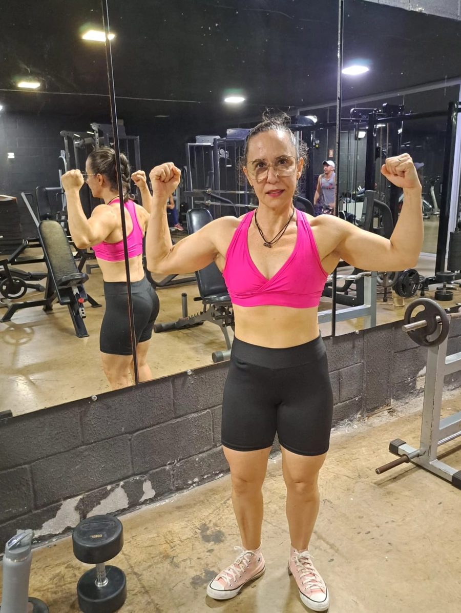 Delma flexionando os braços diante do espelho da academia