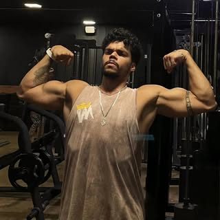 Patrick Matheus, personal trainer, posando na academia com os braços flexionados