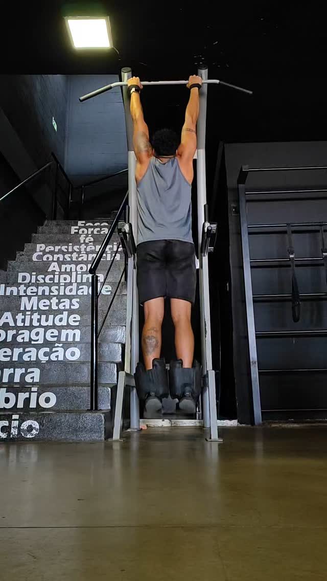Aluno fazendo barra fixa na academia, com parede de palavras: força, disciplina, constância